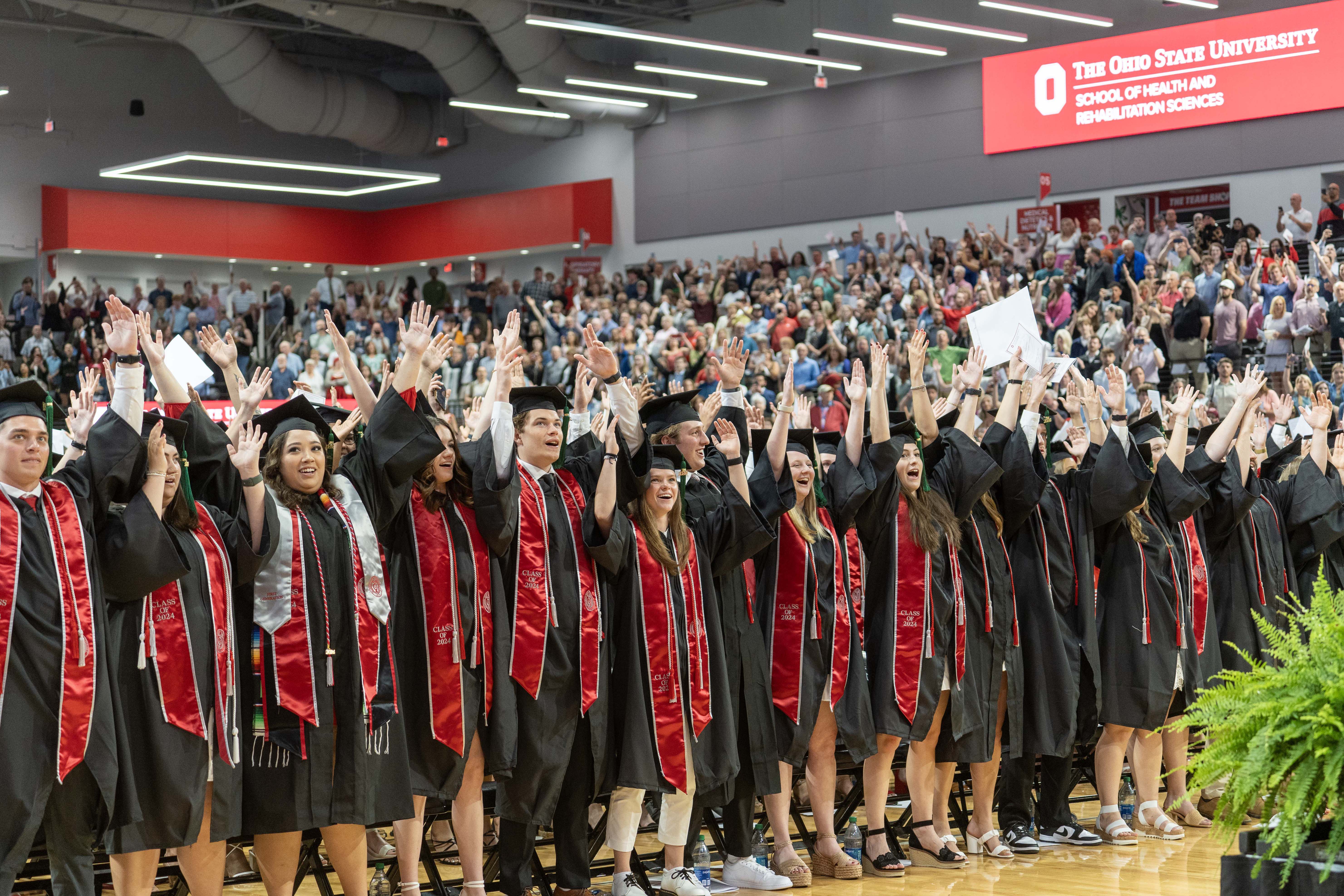 Graduates wearing caps and gowns celebrate at a commencement ceremony in a packed auditorium at The Ohio State University.