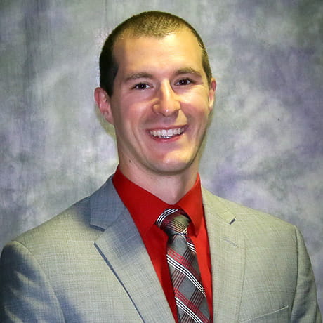 Headshot of Matt smiling wearing gray tux with red shirt 
