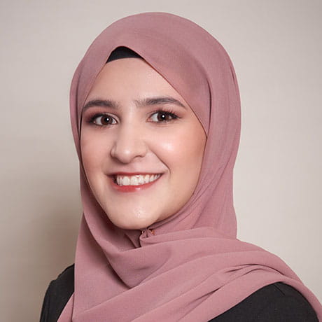 Headshot of Sundus smiling wearing black shirt and pink hijab