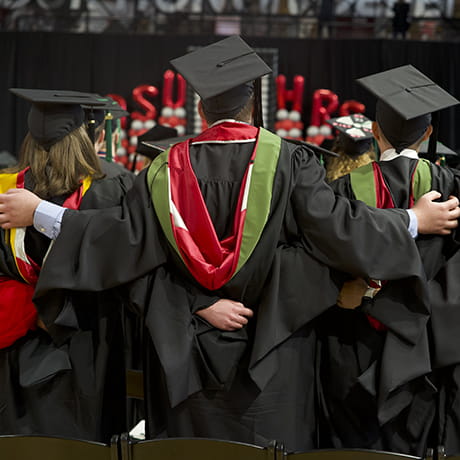 3 graduates in caps and gowns facing away from the camera and towards the stage