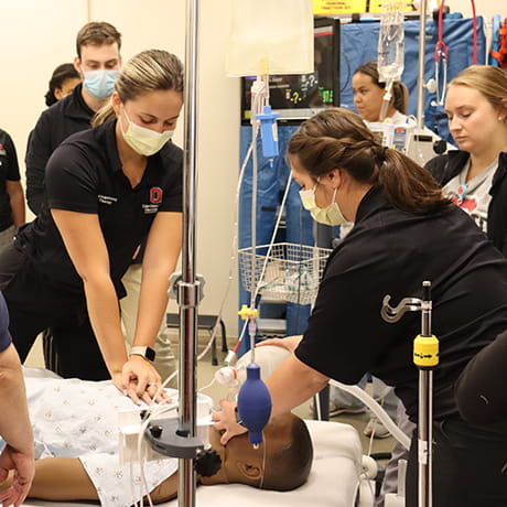 Multiple students watching 2 students and an instructor perform CPR on a patient simulator