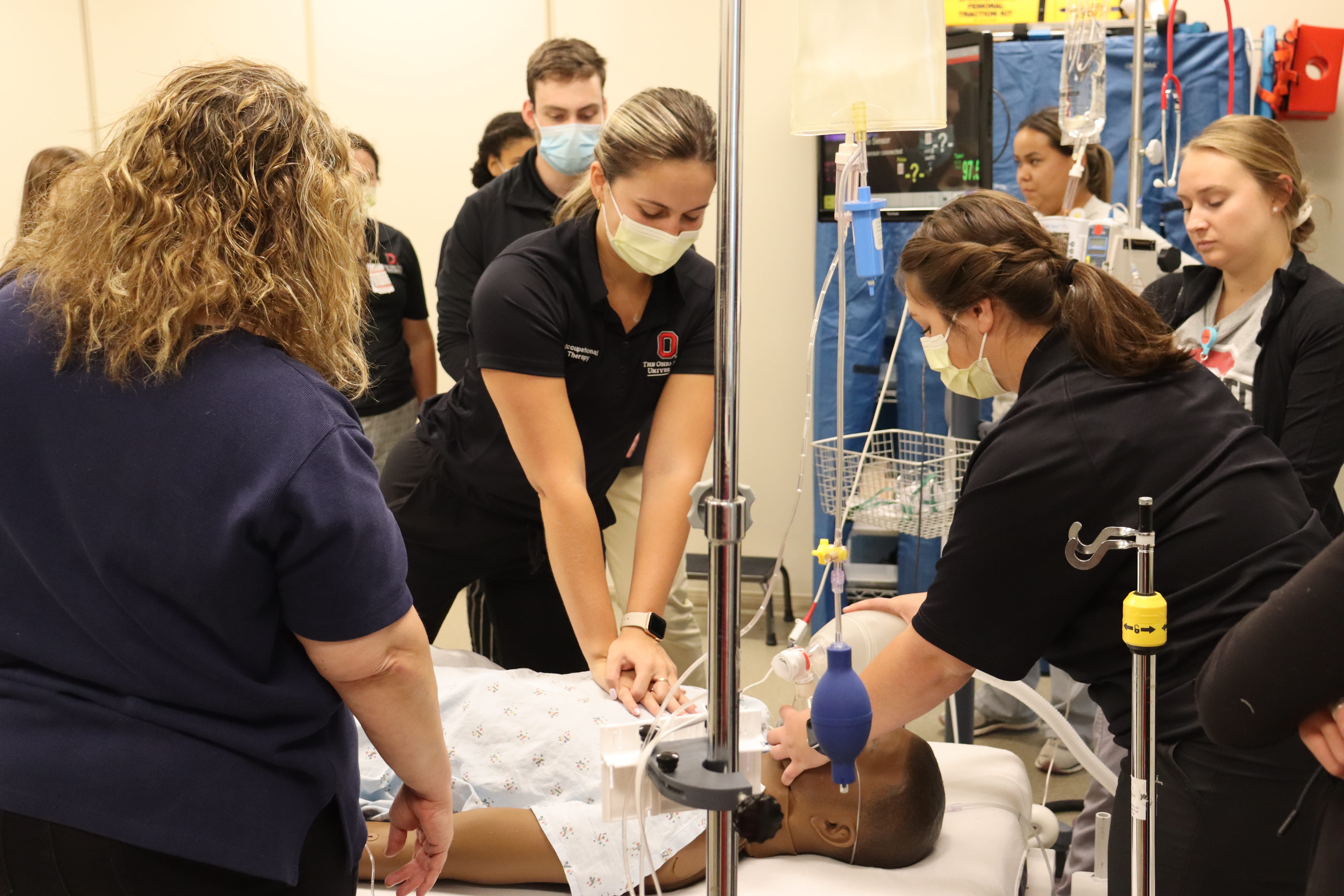 Multiple students watching 2 students and an instructor perform CPR on a patient simulator