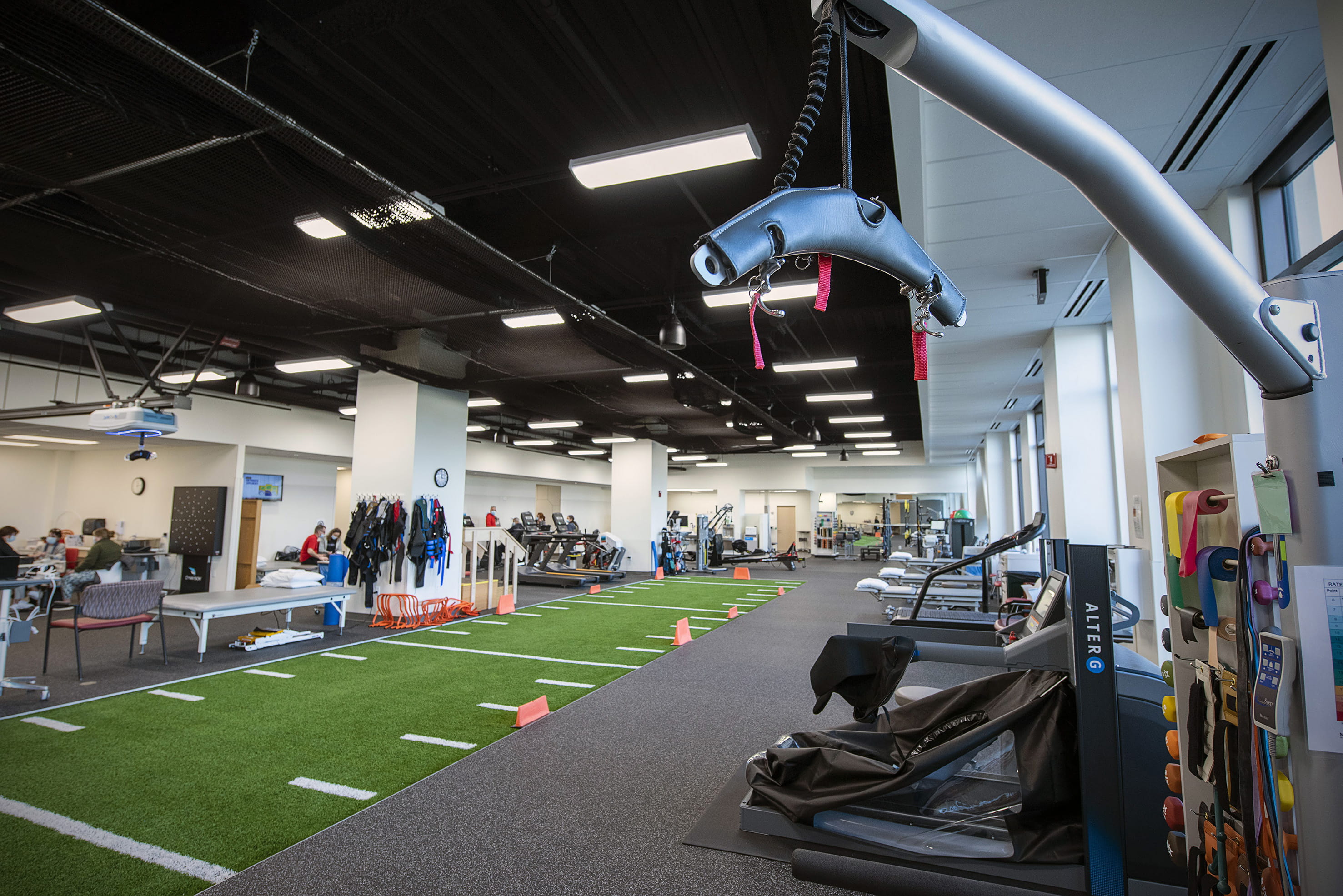 Interior of a spacious, modern gym with various fitness equipment including treadmills, weight machines, and an indoor track. Visible are areas for strength training and functional fitness.