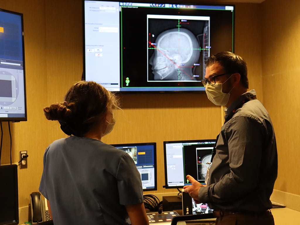 A Radiation Therapy Instructor talking with a student in front of computers showing scans of a head.