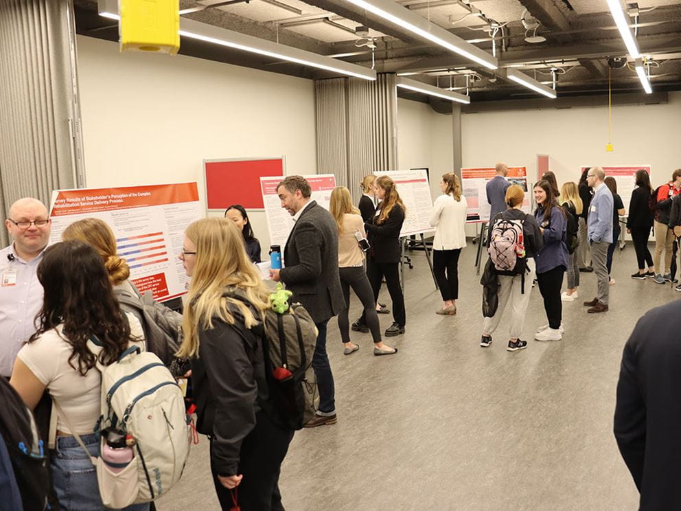 Students and faculty mingling in a room with research posters.