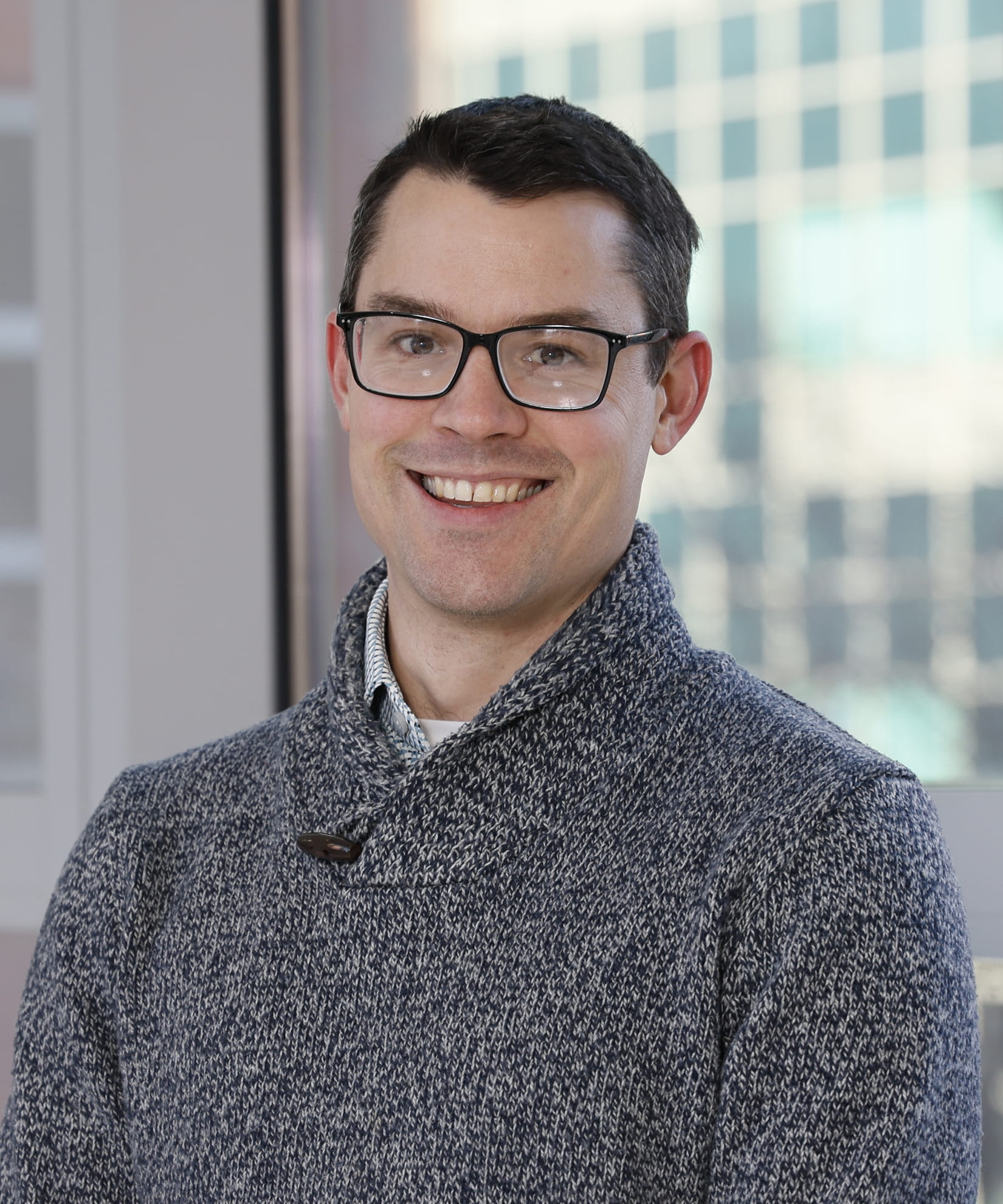 Matthew Husband posing in a well lit area with windows behind him.