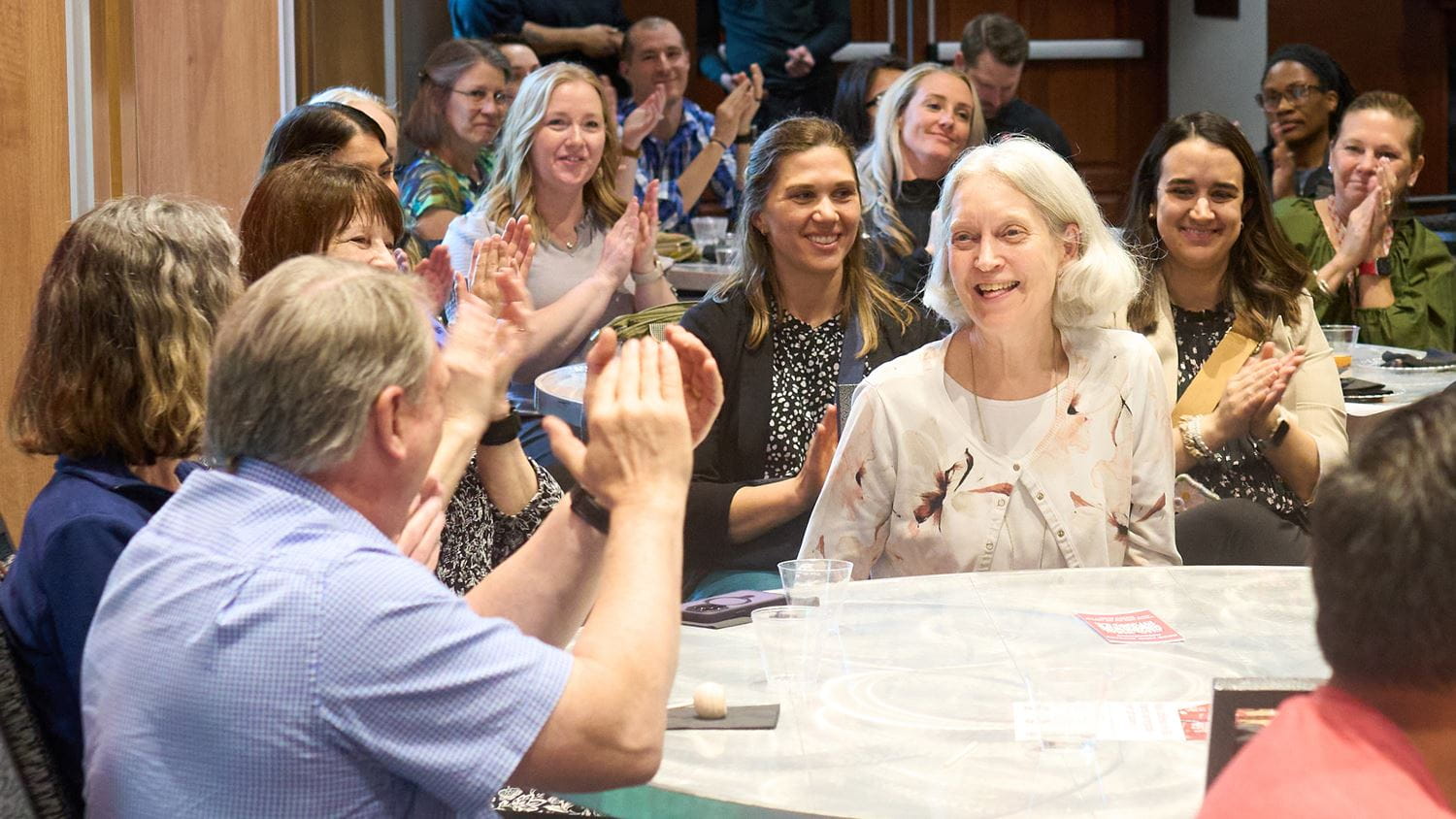 A group of people in an auditorium looking at and clapping for a woman in the center of the room.