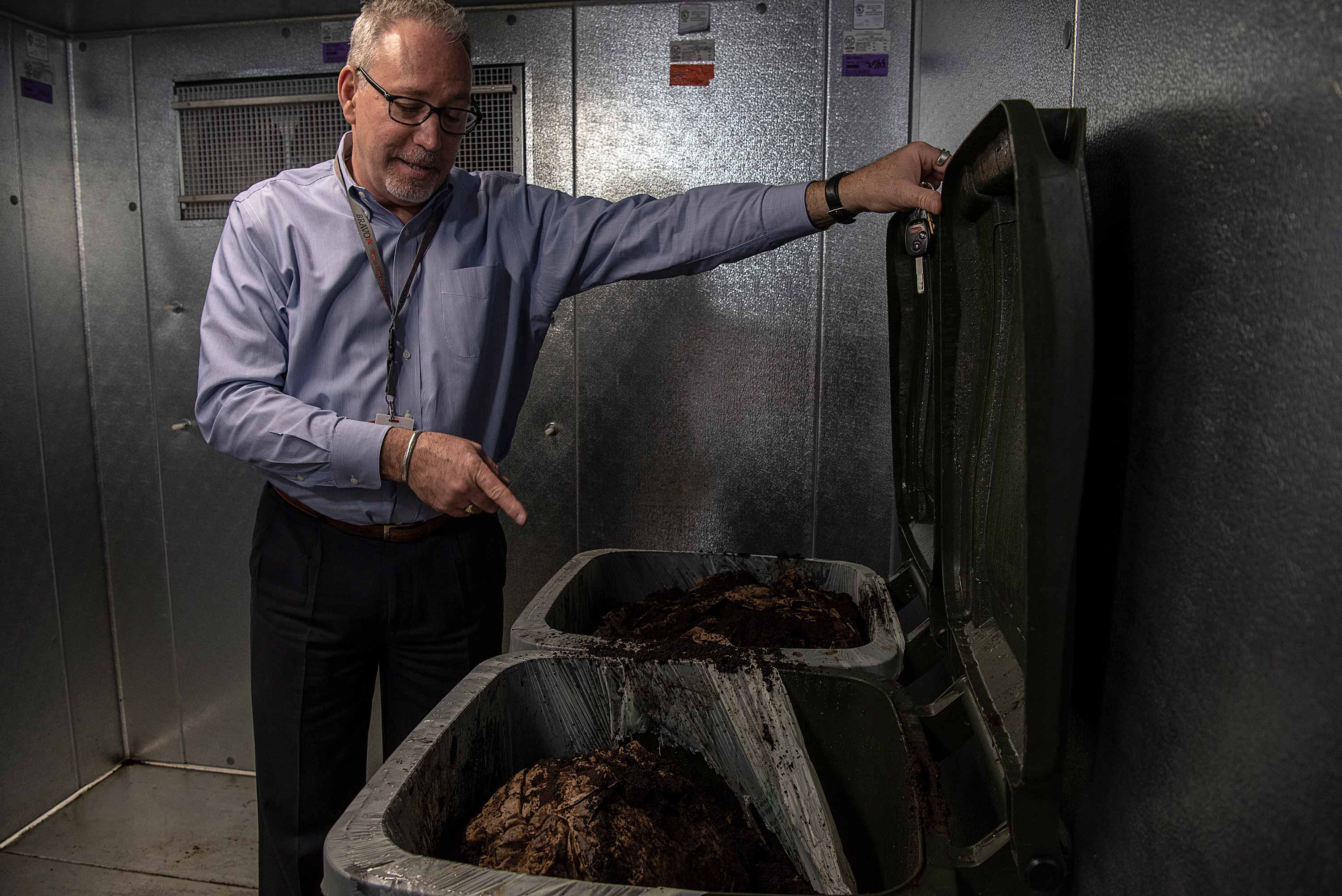 Jim Warner, program director of Food Services Administration, opens 45-gallon totes holding coffee grounds headed to become compost